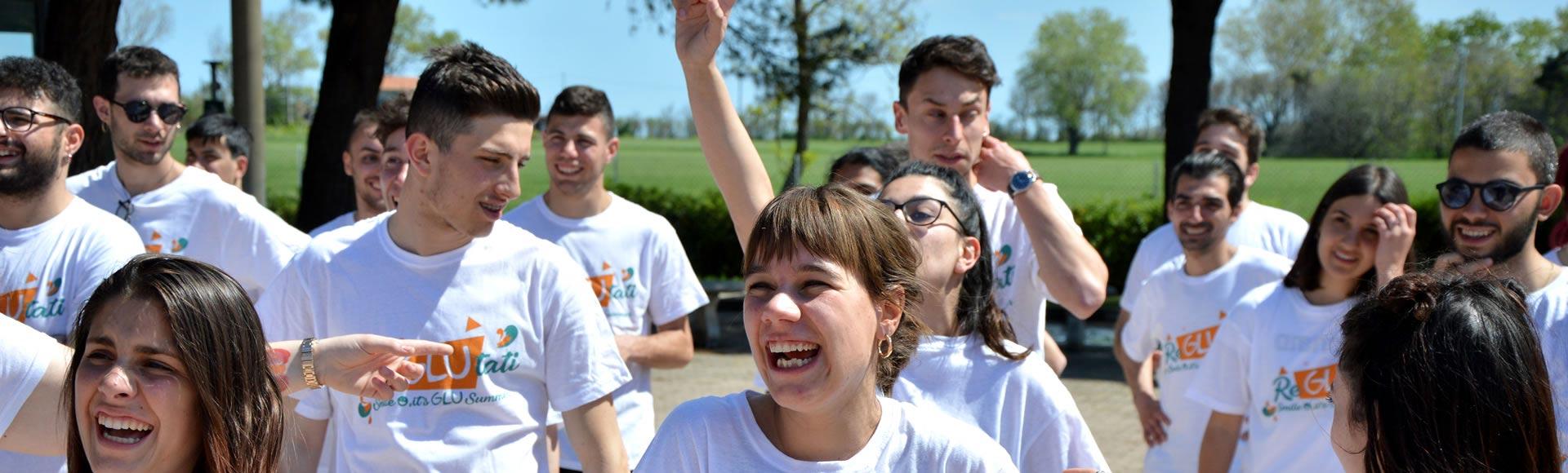 Gruppo di giovani sorridenti indossa magliette bianche durante un evento all'aperto.