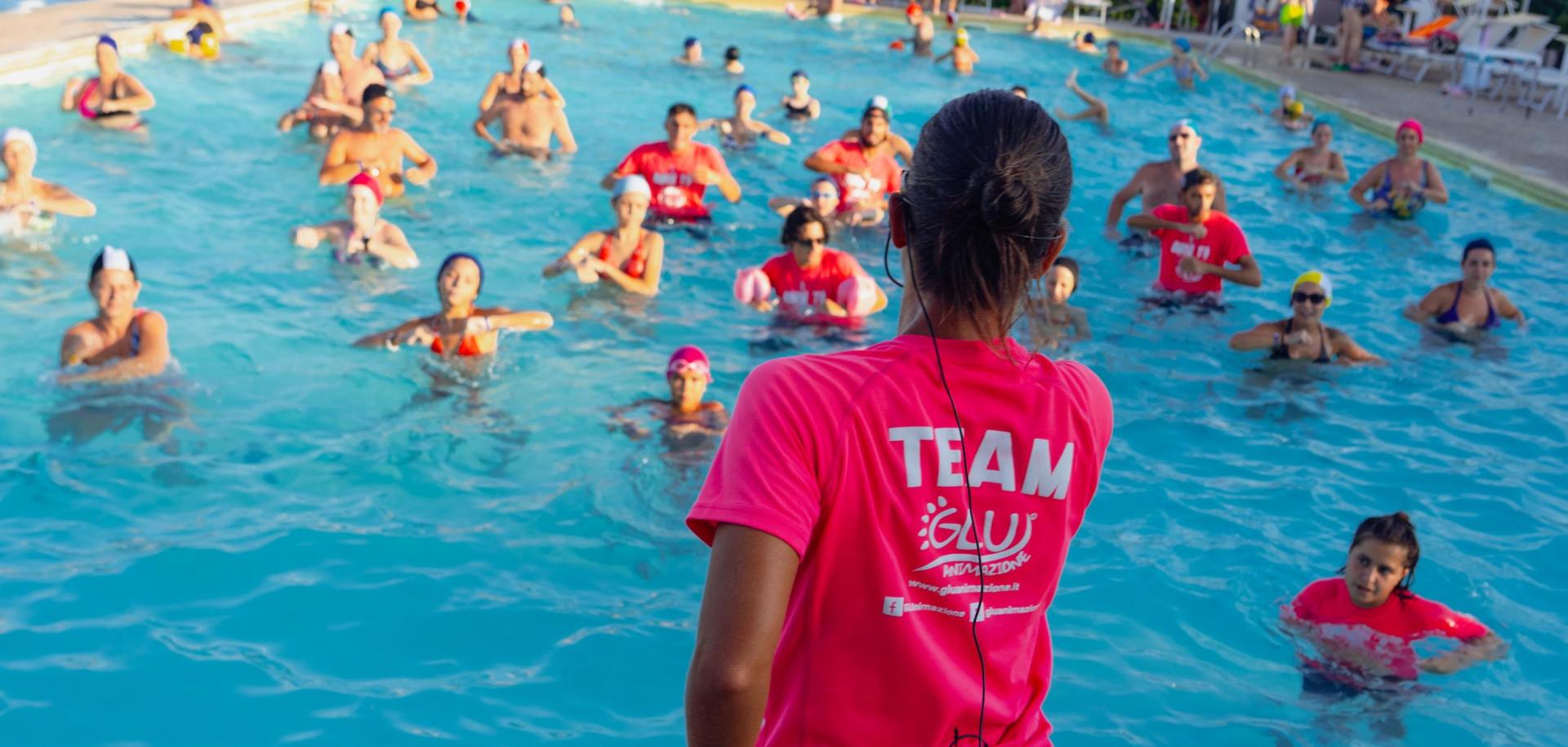 Lezione di acquagym in piscina con istruttore e partecipanti in acqua.